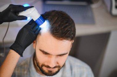 Dermatolog ya da trikoloğun erkek hastanın kafasını alopecia tedavisi için özel bir teşhis aletiyle muayene etmesi