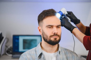 Trikoloğum, saç dökülmesi tedavisi sırasında erkek bir hastanın kafa derisini ve saçını kontrol ediyor.