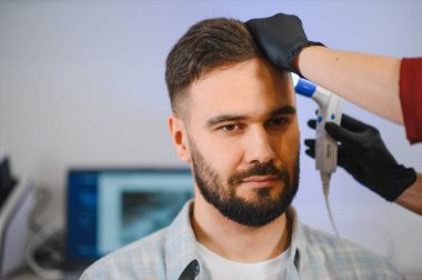 Hasta trikolojik danışmanlık için kliniğe gidiyor. Saç ve kafa derisini teşhis cihazıyla inceleyen bir uzman.