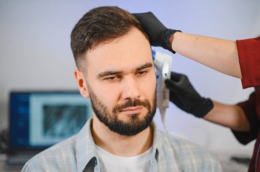 Erkek müşteri, özel bir cilt ve saç analizi cihazı kullanarak bir trikoloğa saç kaybı muayenesi yapıyor.