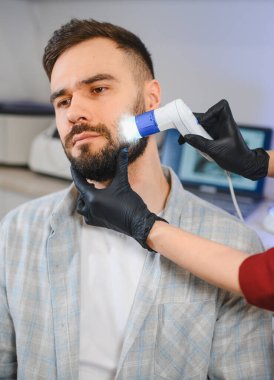 Sağlık analizi için modern bir dermatoskopi cihazı kullanan bir adamın yüzündeki deri ve saç köklerini inceleyen doktor.