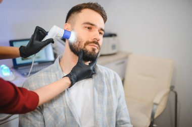 Erkek hasta, profesyonel bir klinikte sakal ve saç sağlığı için detaylı bir trikoskopi muayenesinden geçiyor.