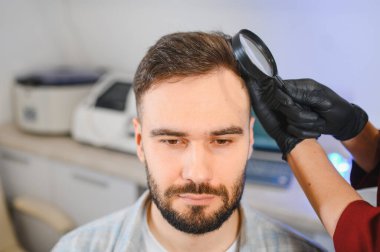 Hasta, saç sağlığı ve kel kalıplarını kontrol etmek için büyüteçle detaylı bir trikoloji muayenesinden geçiyor.