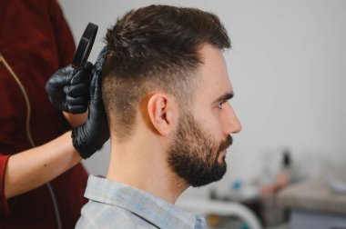 Profesyonel bir dermatolog, genç bir adamın kafa derisinde ben ve cilt kanseri belirtilerini kontrol etmek için büyüteç kullanıyor.