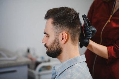 Dermatolog, erkek hastanın alt başındaki beni büyüteçle kontrol ediyor. Cilt kanseri önleme danışmanlığı