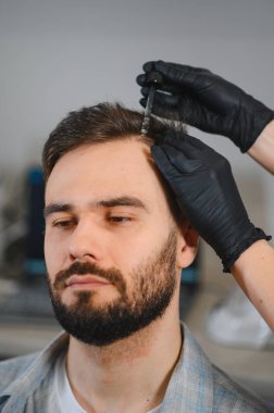 Adam saç yenileme prosedüründen geçiyor. Bir profesyonel, saç bakımı için doğrudan kafa derisine serum uygulamak için pipet kullanır.