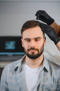 Genç bir adam eldivenli bir uzmandan saç dökülmesi tedavisi serumu alıyor. Alopecia sorunlarına değiniyor.