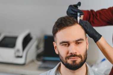 Genç adam saç dökülmesi sorunu için kafa derisi aşısı oluyor. Profesyonel trikoloğum saç büyümesi için tıbbi prosedür uyguluyor.