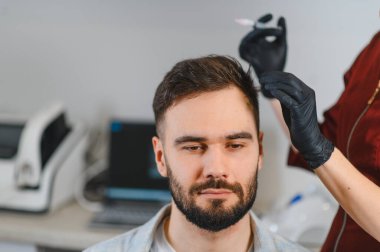 Bir trikoloğun kafa derisine iğne yaptığı bir adam. Klinikteki saç büyümesi ve alopezi sorunlarını ele alıyor.