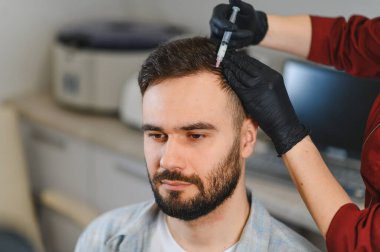 Genç bir adam saç dökülmesini önlemek ve saç uzamasını hızlandırmak için doktordan reçete ya da mezoterapi iğneleri alıyor.
