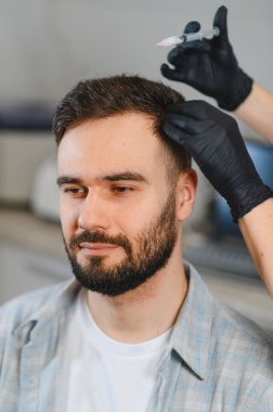 Genç bir erkek hasta, özel bir doktorla klinikte saç restorasyonu ve kafa derisini yenilemek için mezoterapi görüyor.