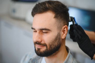 Adamın saç ve kafa derisini profesyonel dermatoskop uzmanı analiz ettiriyor. Saç dökülmesi tedavisi için tıbbi prosedür