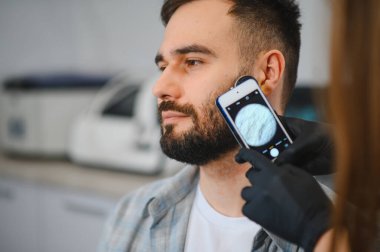 Doktor, adamın derisini gezici dermatoskopi ile kontrol ediyor. Benleri ve deri sorunlarını tarıyor.