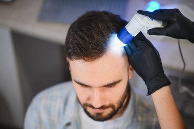 Trikoloğum bir adamın kafa derisini modern bir trikop ile inceliyor, saç kaybını teşhis ediyor ve tedavi ediyor.