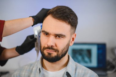 Saç dökülmesi ya da cilt hastalıklarını teşhis etmek için özel ekipman kullanan bir trikoloğun kafa derisi ve saç muayenesinden geçen hasta.