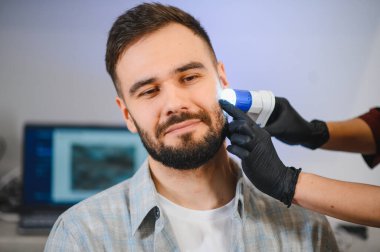 Erkek hasta dermatoskop kullanarak doktordan ben taraması alıyor. Tıbbi uzman erken teşhis için cilt sağlığını kontrol ediyor