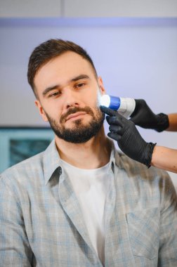 Profesyonel bir dermatolog, bir sağlık kliniğinde bir adamın cildini dermatoskopla inceliyor. Dermatoloji ve cilt sağlığı kavramı