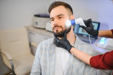 Hasta, sakal ve özel bir aletle profesyonel trikoloji muayenesi yaptırıyor, saç ve cilt bakımı alıyor.