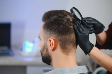 Dermatolog, hastanın kafasını büyüteç kullanarak, benleri, deri durumlarını ve olası sorunları kontrol ediyor.