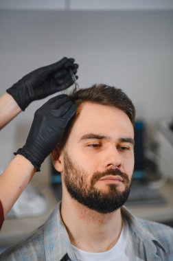 Trikoloji kliniğinde saç yenileme tedavisi gören bir adam. Doktor kelliği önlemek için kafa derisine sıvı uyguluyor.