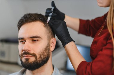 Erkek hasta, saç dökülmesini ya da kelliği tedavi eden bir dermatologdan kafa derisine kozmetik mezoterapi yaptırıyor.