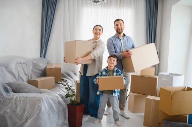 Aile gülümsüyor ve karton kutuları parlak yeni bir dairede taşıyor, taşınma gününü ve yeni bir hayatın başlangıcını kutluyorlar.