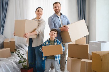 Gülümseyen ebeveynler ve çocuk ellerinde karton kutular, taşınmayı kutluyorlar ve yeni evlerini dört gözle bekliyorlar.