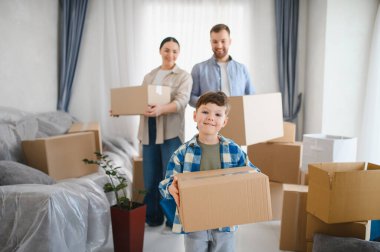 Taşındıktan sonra bavulları boşaltan mutlu bir aile. Ebeveynler ve çocuklar taşınan kutularla aydınlık bir odada duruyorlar.