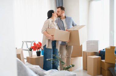 Mutlu çift yeni evlerini taşınma gününde kutluyorlar, kutular ve ev eşyalarıyla çevrili, sevgiyi kucaklıyorlar.