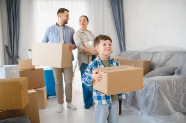 Yeni evlerine karton kutular taşıyan genç bir aile yeni bir başlangıcı ve yeni bir yeri mutlulukla kutluyorlar.