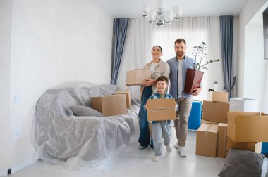 Mutlu bir aile yeni bir eve taşınıyor, karton kutular ve bir bitkiyi parlak, ferah bir odaya taşıyor.