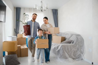 Genç bir aile, anne baba ve oğul, karton kutular ve bir bitki taşıyorlar, yeni evlerine taşınıyorlar ve yeni bir başlangıç yapıyorlar.