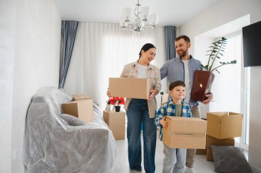 Ebeveynler ve çocuklar karton kutular taşıyorlar, bir çiçek, ve yeni dairelerine taşınırken mutluluğu hissediyorlar.