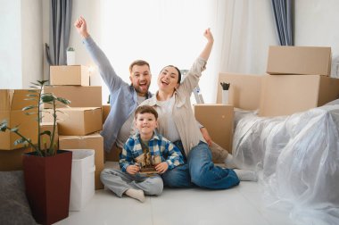 Karton kutular ve kişisel eşyalarla çevrili yeni bir eve taşınmayı kutlayan çocuklu heyecanlı bir aile.