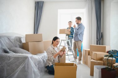Ebeveynler ve çocuklar gülümsüyor, karton kutuları ve ev eşyalarını açıyor, yeni bir aile hayatı için yenilenmiş mülke yerleşiyorlar.