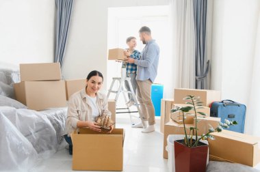 Mutlu aile karton kutulardan kişisel eşyalarını boşaltıyor, taşındıktan sonra yeni geniş bir apartman dairesine yerleşiyor.