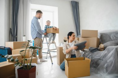 Aile bireyleri ve çocuklar karton kutuları birlikte paketliyor, yeni evlerine taşınıyorlar, değişiklikten dolayı mutlular.