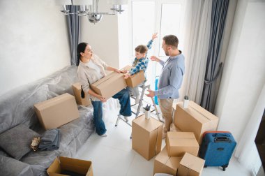 Ebeveynler ve oğulları yeni evlerine yerleşirken gülümseyen parlak, modern bir apartman dairesinde kutuları açıyorlar.