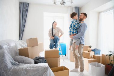 Aile oturma odasında kutuları açıyor, gülümsüyor ve kucaklıyor, taşınmayı kutluyor ve yeni bir başlangıç yapıyor.