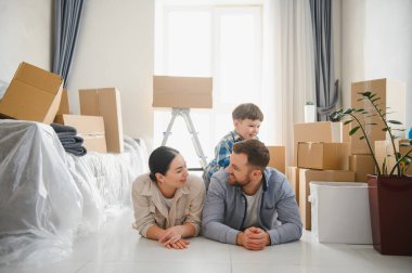 Mutlu bir aile, taşındıktan sonra karton kutularla çevrili yeni dairelerinde yerde yatıyor.