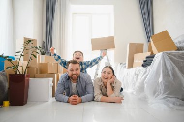 Karton kutularla çevrili, yerde oğluyla gülümseyen genç bir aile yeni evlerine taşınmayı kutluyorlar.