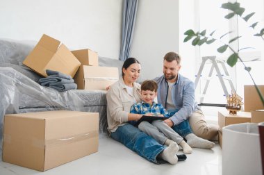 Genç bir aile, aileler ve çocuklar, karton kutularla çevrili yerde oturuyorlar, yeni bir eve taşınmayı planlıyorlar.