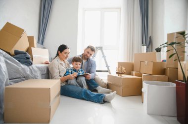 Çocuklu bir aile karton kutuların arasında oturmuş, yeni bir daireye ya da eve taşınmaya hazırlanıyor.