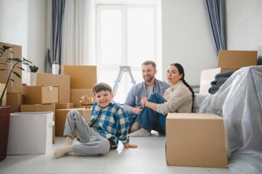 Bir çocuk, yerde oturan aileler, yeni dairelerine taşındıktan sonra etrafları karton kutularla çevrili.