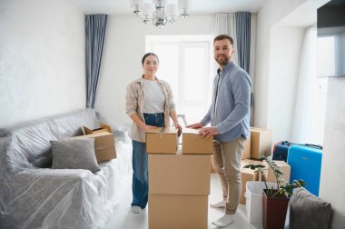 Genç çift gülümsüyor, yeni bir evde karton kutular düzenliyorlar. Yerleştirme ve mülkiyet mülkiyeti kavramı