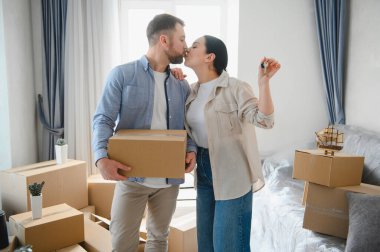 Genç çift yeni bir eve sahip olmalarını kutluyorlar. Karton kutuları modern dairelerinde taşıyorlar ve öpüşüyorlar.