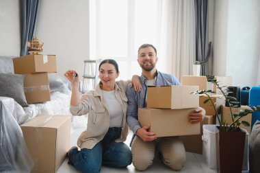 Yeni bir ev almamızı kutlayan gülümseyen bir çift. Adam kutuları taşıyor, kadın yeni evin anahtarlarını tutuyor.