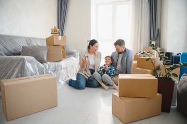 Aile taşınıyor, aileler ve çocuklar yerde oturuyor kutuları taşıyorlar, yeni evlerini kutluyorlar.