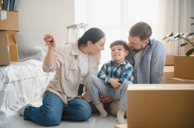 Karton kutularla çevrili mutlu bir aile ve küçük bir çocuk yeni evlerinin tadını çıkarıyorlar. Annem evin anahtarlarını tutuyor.