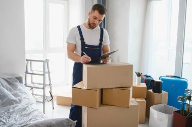 Bir apartmanda duran profesyonel nakliyeci, bir ev taşıma ve paketleme servisi sırasında envanter listesini bir panoda kontrol ediyor.